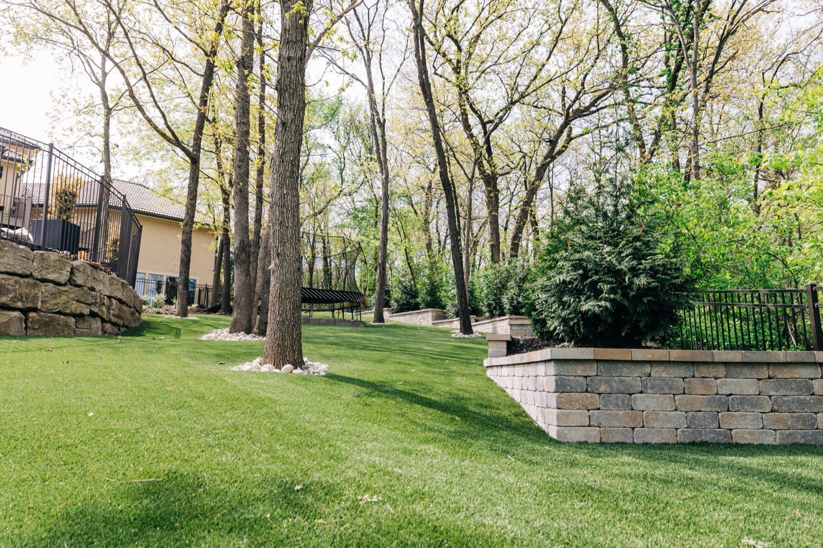 Premium ForeverLawn synthetic turf residential install with stone retaining wall and mature trees in the Kansas City metro